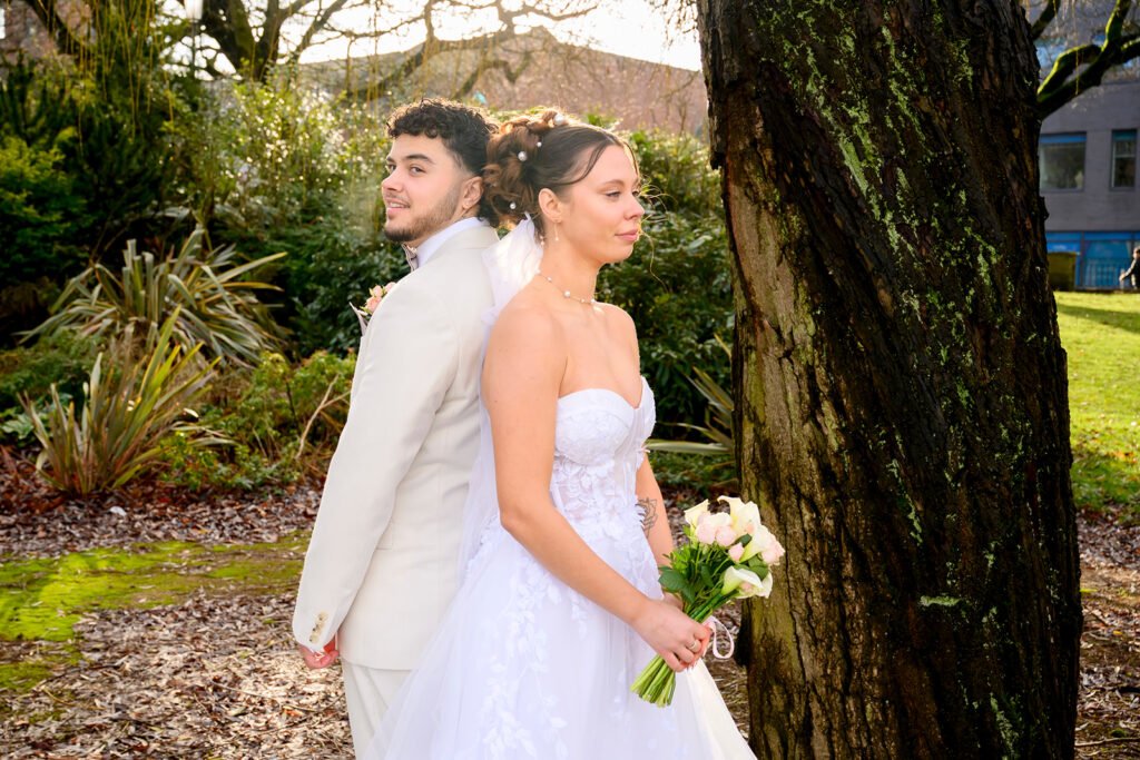 Romantic portrait of a bride and groom leaning against a tree in a West Midlands park.